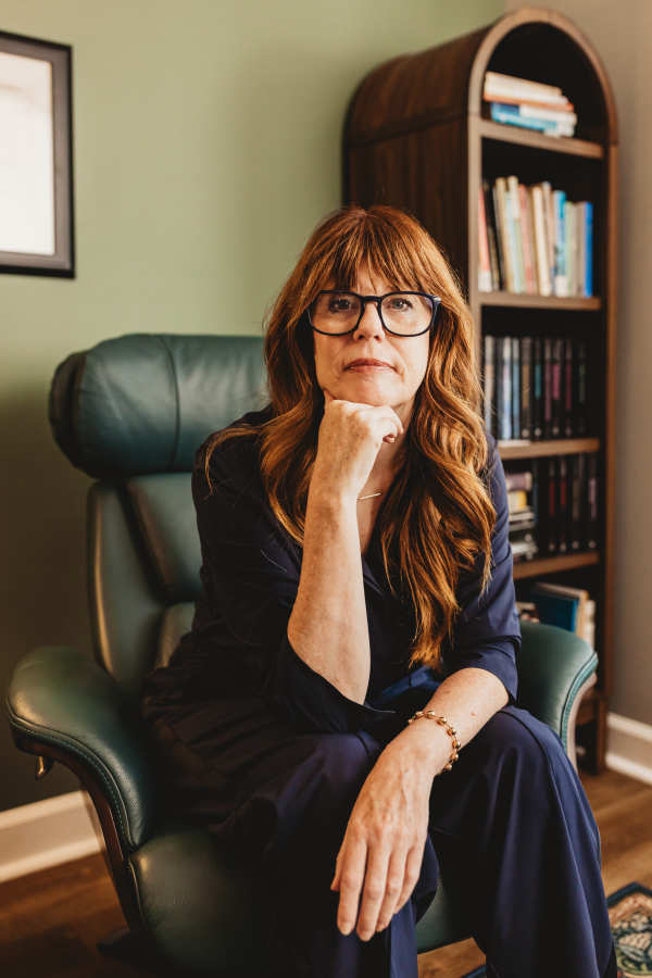 Lisa Giebelhaus seated in a green leather chair beside an arched bookcase, hand resting at her chin